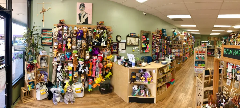 Panoramic view of a pet store with plush toys, pet supplies, and a checkout counter on a wood floor.