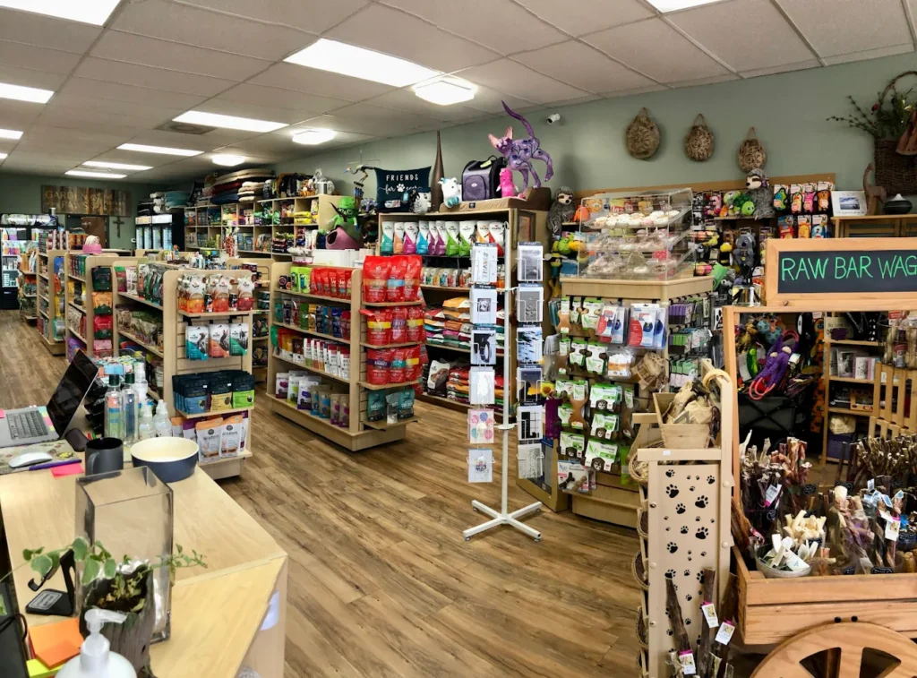 A pet supply store interior with organized shelves of pet food, toys, and accessories on a wooden floor.