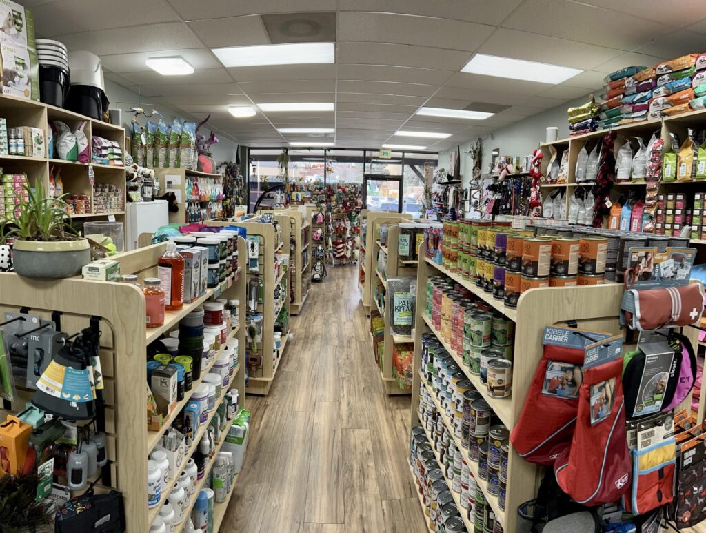 A pet supply store aisle with shelves stocked with pet food, toys, and accessories, viewed from the entrance.