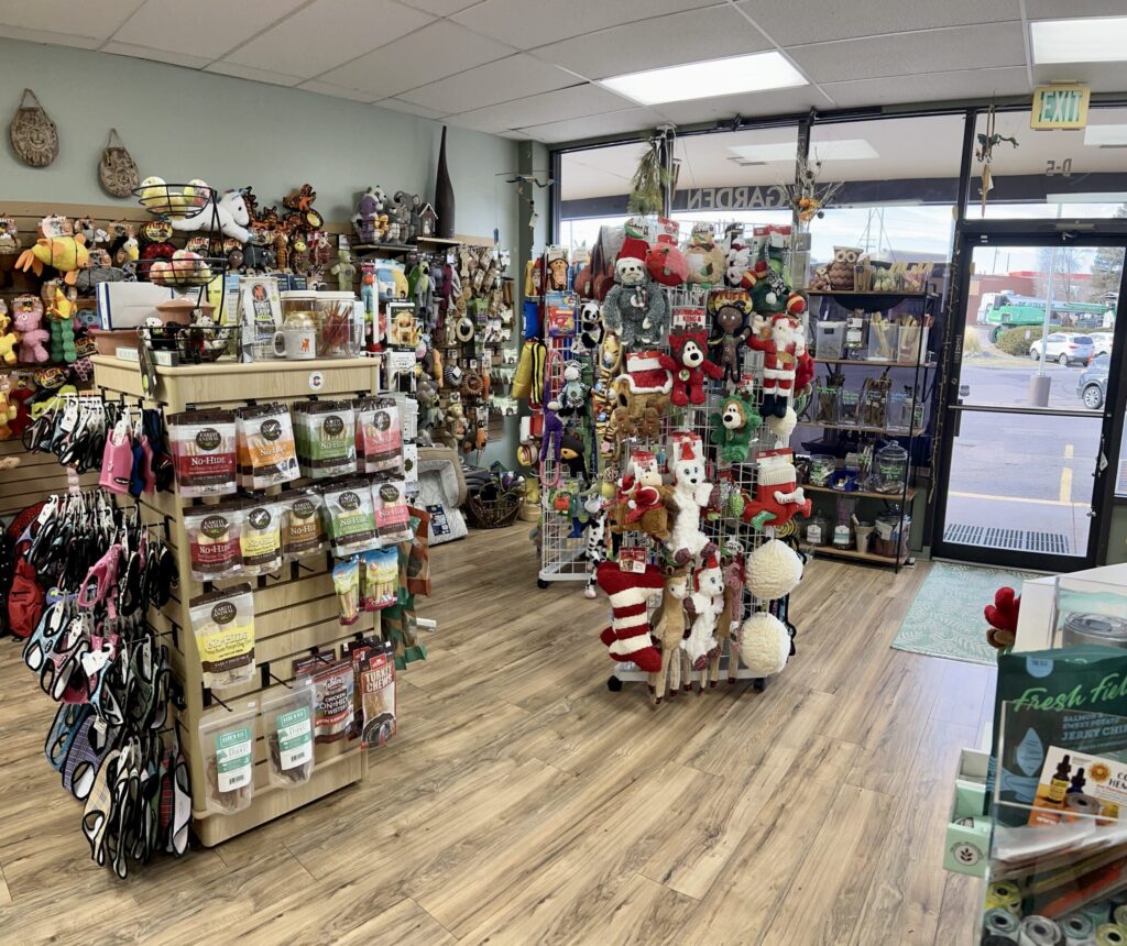Pet store interior with shelves of pet supplies, toys, treats, and holiday-themed plush toys near the entrance.