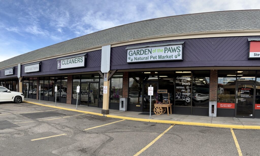 Strip mall storefronts including a dry cleaner and "Garden of the Paws" natural pet market, with parked cars in front.